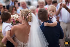 On the steps outside the church in L'Isle Jourdain, the bride and groom are seen from behind as they each carry a toddler in their arms, walking away together just after concluding their religious ceremony.